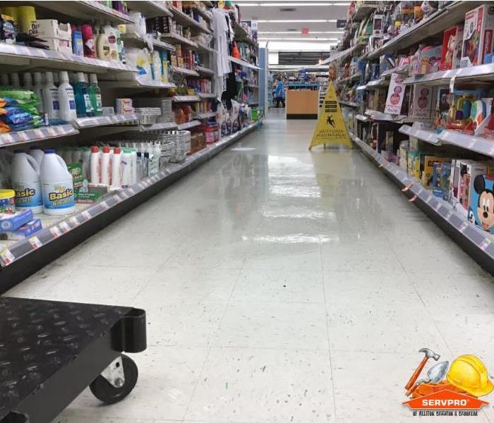 The floor in an isle of a local Walgreens store has a puddle of water and a caution sign is warning customers of wet area. 