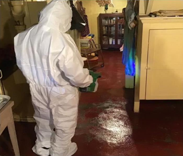 technician in protective white suit sprays room 